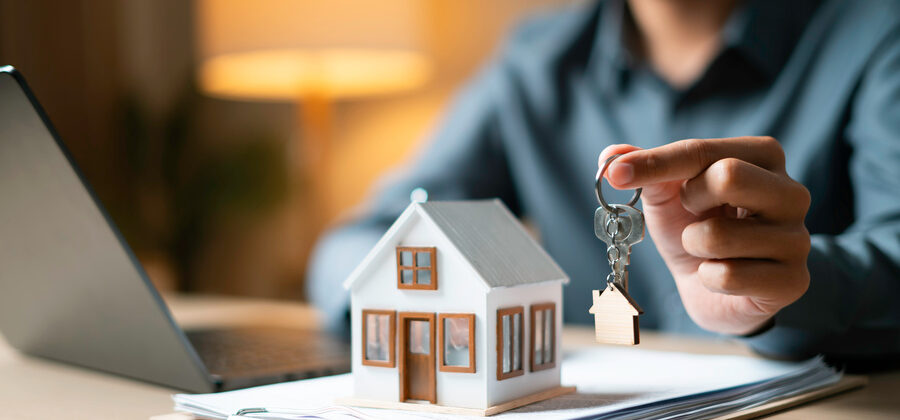 real estate agent hand presenting house-shaped keychain and model house, symbolizing closing on a new home
